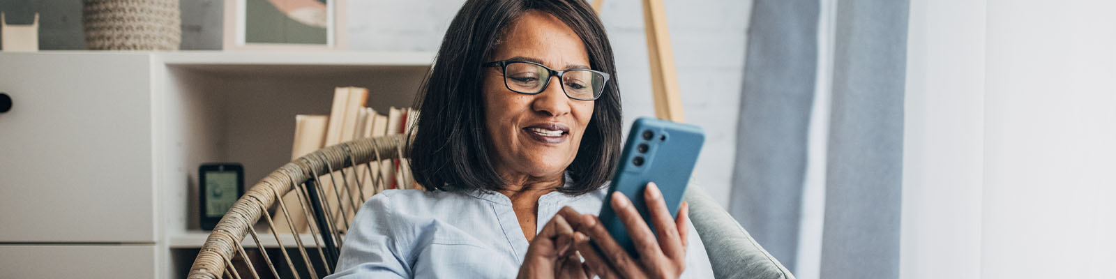 A senior woman sitting in a wooden chair smiling and looking down at her phone