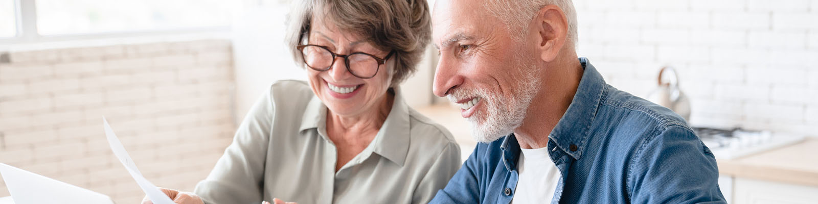 A senior man and woman sitting at a table looking down at a laptop