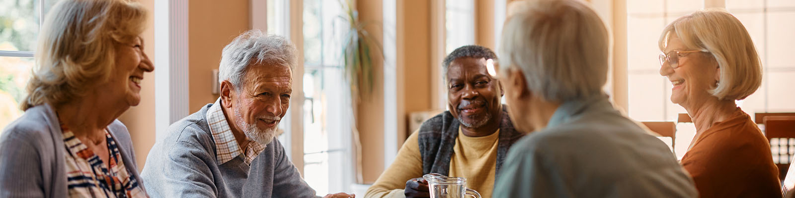 A group of senior men and women having dinner at a table in the dining room at a senior living facility