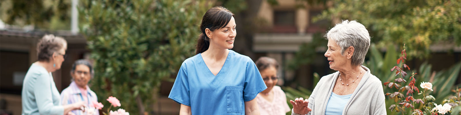 A senior woman walking outside at a senior living facility with her nursing assistant