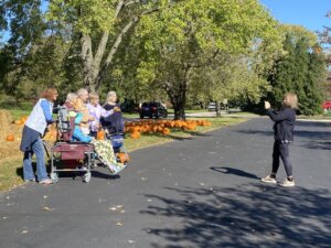 Photo of the Traditions activity director taking a photo of seniors outdoors at a Fall event